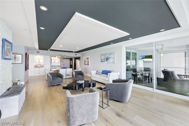 living room with a raised ceiling, ceiling fan, and light hardwood / wood-style flooring