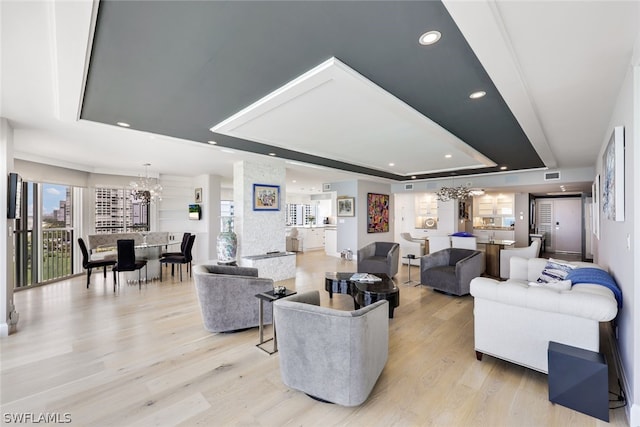 living room with a tray ceiling, a chandelier, and light hardwood / wood-style flooring