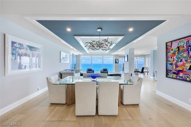 dining area with a chandelier, light hardwood / wood-style floors, and a raised ceiling