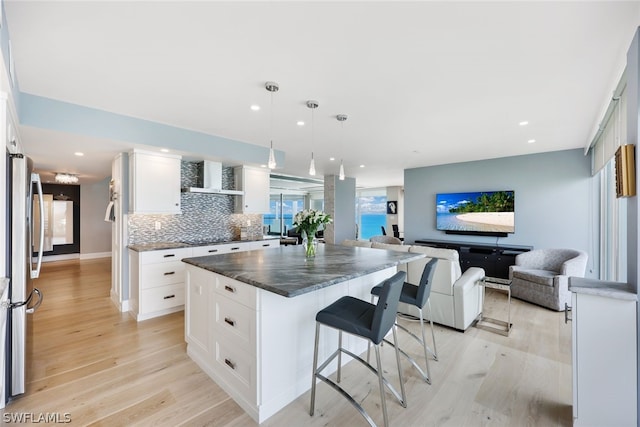 kitchen with pendant lighting, white cabinets, wall chimney exhaust hood, tasteful backsplash, and stainless steel refrigerator