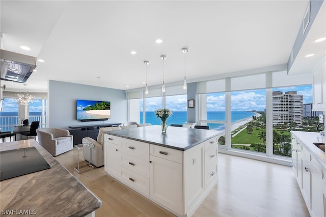 kitchen featuring a center island, decorative light fixtures, white cabinetry, light wood-type flooring, and expansive windows