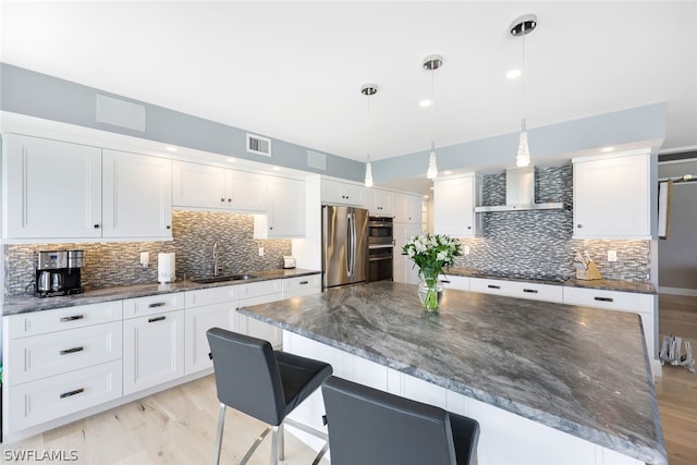 kitchen with appliances with stainless steel finishes, wall chimney exhaust hood, white cabinetry, sink, and hanging light fixtures