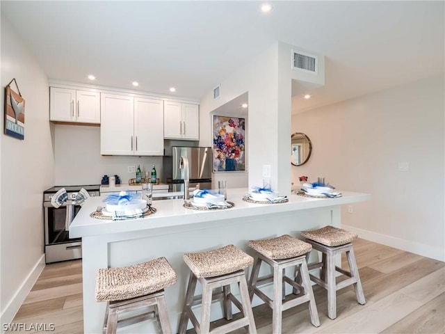 kitchen featuring a kitchen breakfast bar, light hardwood / wood-style flooring, white cabinets, and appliances with stainless steel finishes