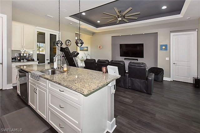 kitchen with dishwasher, ceiling fan, a raised ceiling, a center island with sink, and white cabinets