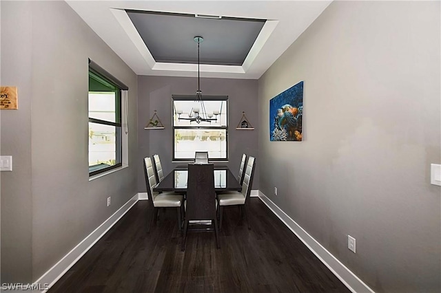 dining room featuring dark wood finished floors, a raised ceiling, a notable chandelier, and baseboards