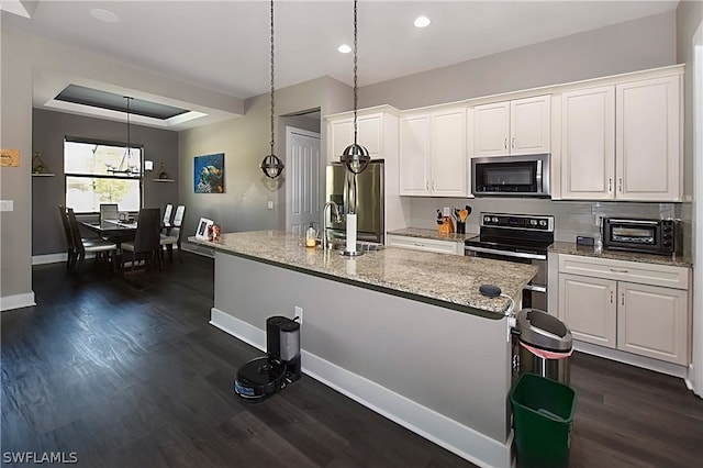 kitchen featuring decorative light fixtures, appliances with stainless steel finishes, white cabinetry, dark hardwood / wood-style floors, and a kitchen island with sink