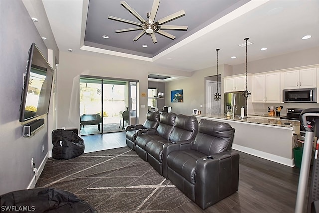 living room with a tray ceiling, dark hardwood / wood-style flooring, and ceiling fan