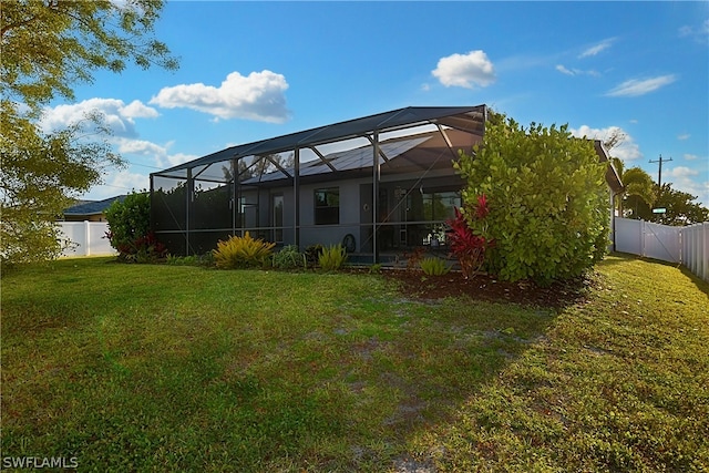 rear view of house featuring glass enclosure and a lawn