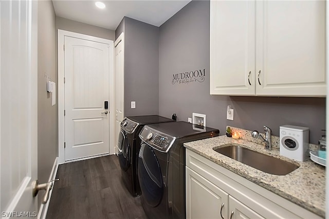 clothes washing area with dark wood-type flooring, cabinets, washing machine and clothes dryer, and sink