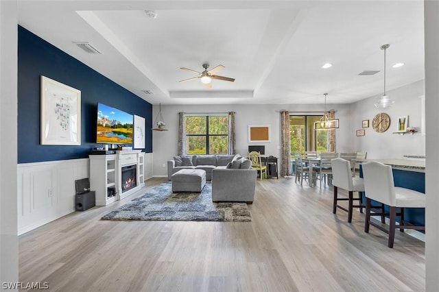 living room with a healthy amount of sunlight, a tray ceiling, and light hardwood / wood-style floors