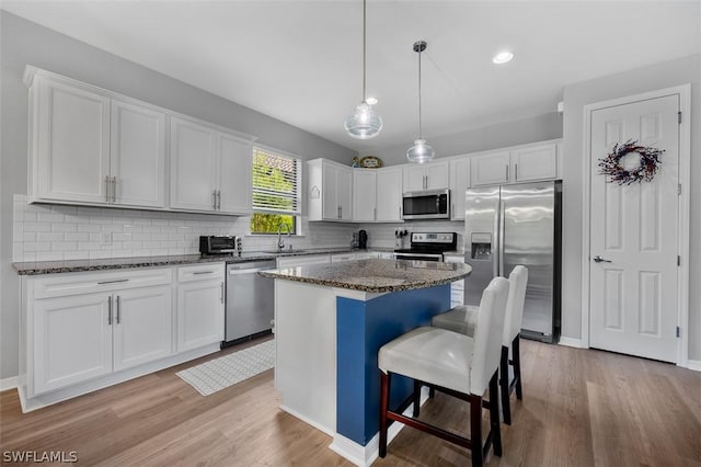 kitchen featuring white cabinetry, stainless steel appliances, dark stone countertops, and a kitchen island