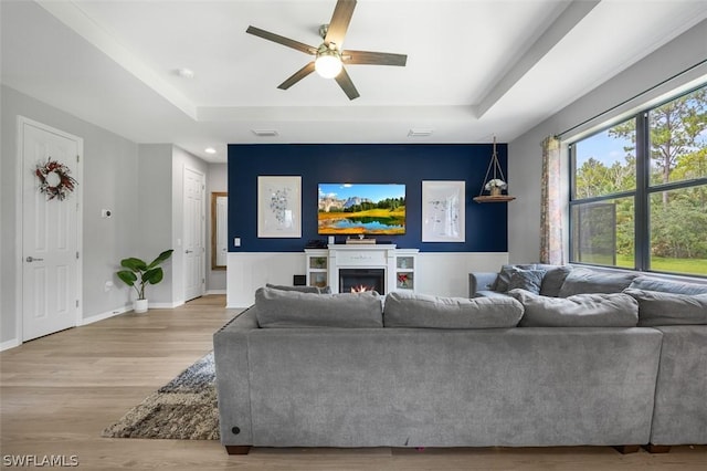 living room with ceiling fan, light wood-type flooring, and a tray ceiling