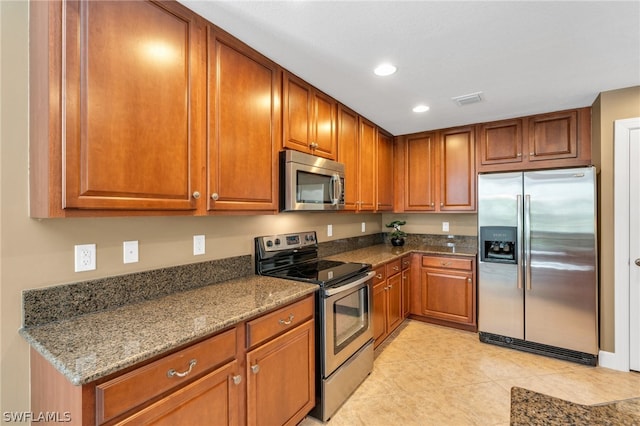 kitchen with stainless steel appliances, dark stone counters, and light tile patterned flooring