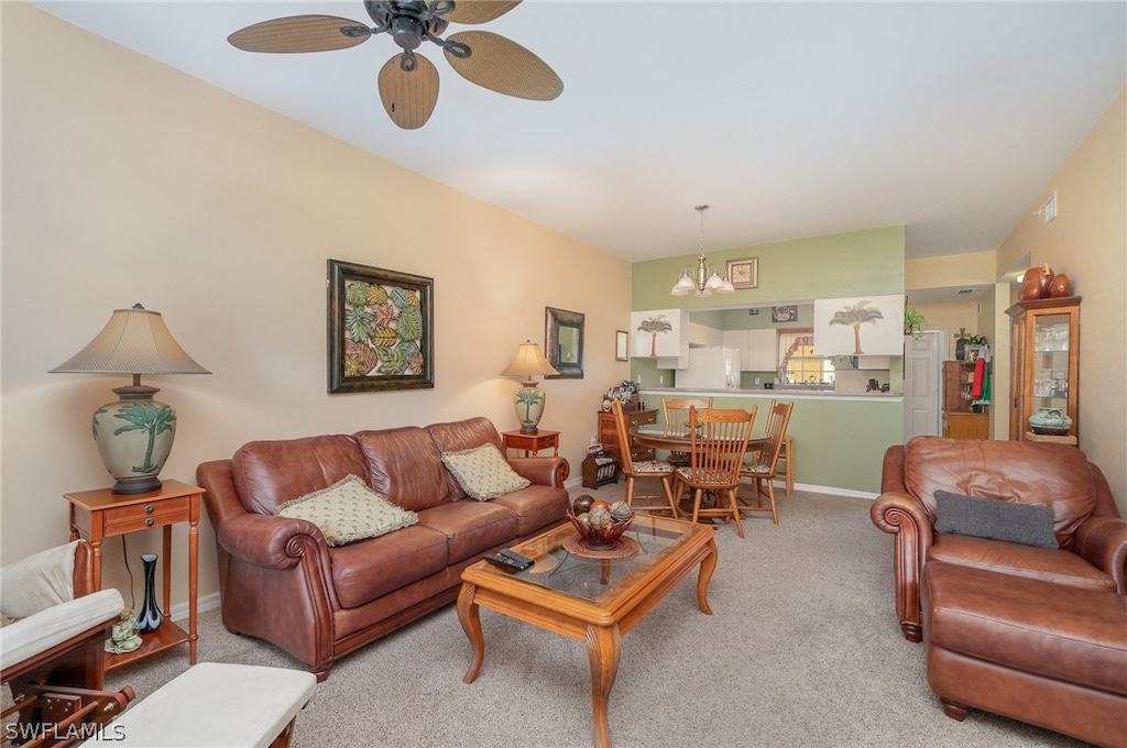 living area with ceiling fan with notable chandelier, baseboards, and light colored carpet