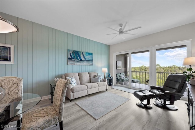 living room featuring light hardwood / wood-style floors, ceiling fan, and wooden walls