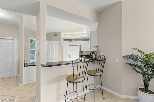 kitchen with a breakfast bar area, white cabinets, kitchen peninsula, light tile patterned flooring, and white fridge with ice dispenser