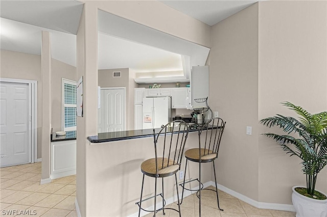 kitchen with light tile patterned flooring, white cabinetry, a kitchen bar, white fridge with ice dispenser, and kitchen peninsula