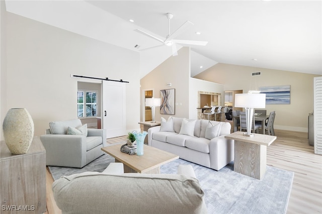 living room with high vaulted ceiling, a barn door, ceiling fan, and light hardwood / wood-style flooring