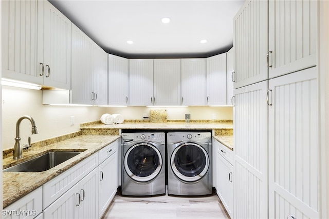 clothes washing area with cabinets, washing machine and dryer, sink, and light hardwood / wood-style floors