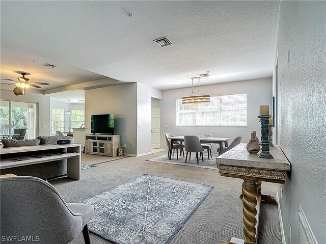 living room with ceiling fan, light colored carpet, and a textured ceiling