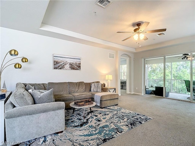 carpeted living room with a raised ceiling and ceiling fan