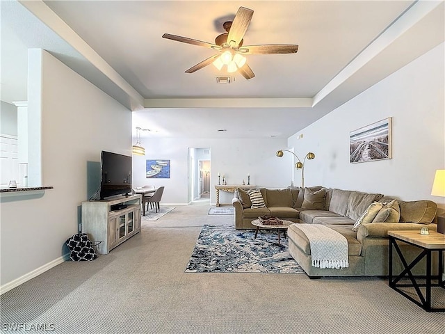living room with ceiling fan, a tray ceiling, and light carpet