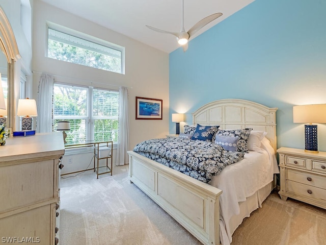 bedroom featuring a towering ceiling, light colored carpet, and ceiling fan