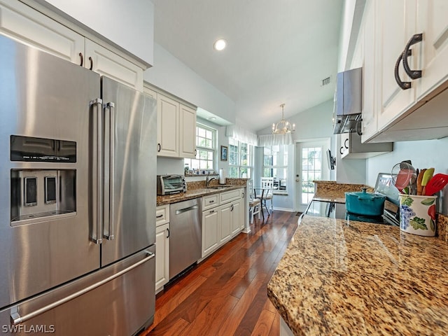 kitchen with white cabinets, sink, hanging light fixtures, light stone countertops, and stainless steel appliances