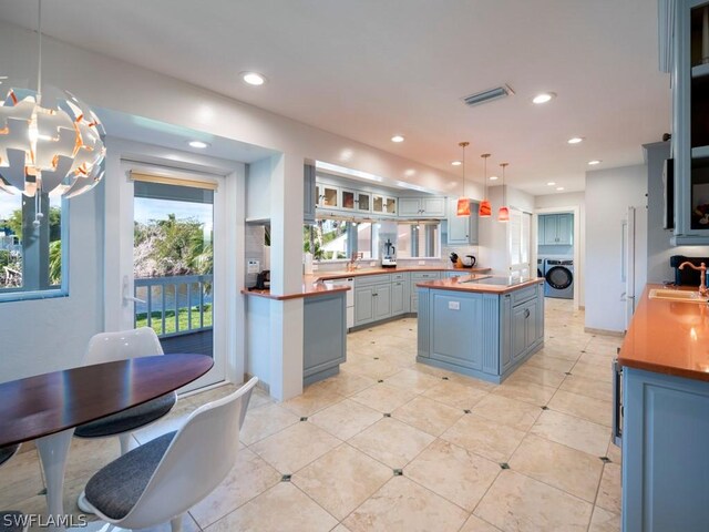 kitchen with pendant lighting, wooden counters, a kitchen island, washer / clothes dryer, and sink