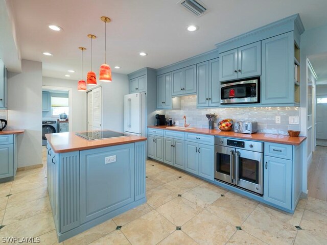 kitchen with a center island, appliances with stainless steel finishes, tasteful backsplash, hanging light fixtures, and washing machine and dryer