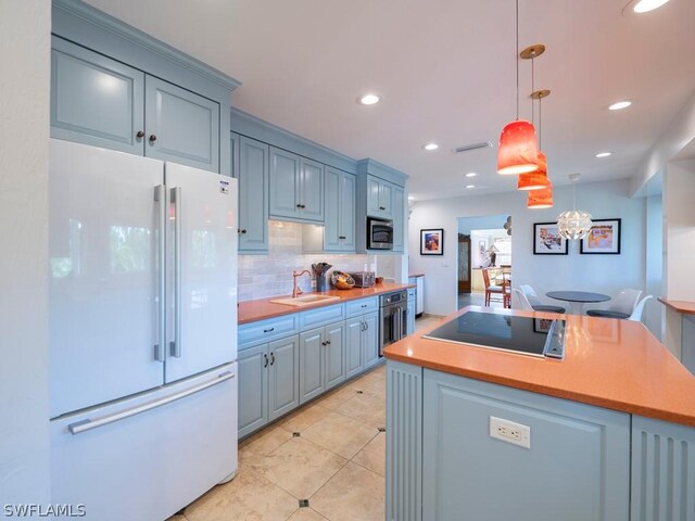 kitchen featuring stainless steel microwave, white fridge, black electric cooktop, sink, and pendant lighting