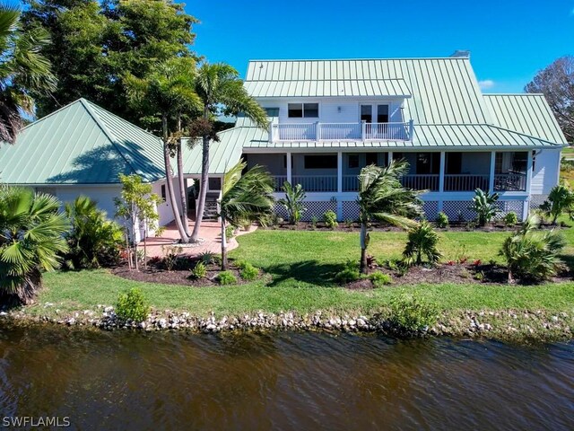 rear view of house featuring a balcony, a water view, and a lawn