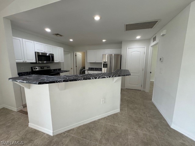 kitchen with light tile patterned flooring, appliances with stainless steel finishes, a kitchen breakfast bar, and white cabinetry