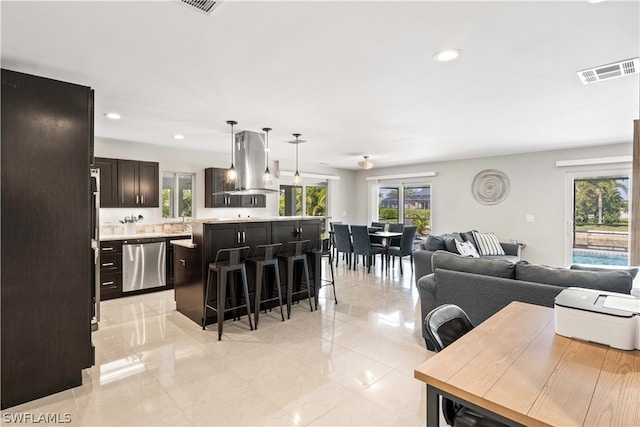 interior space featuring a breakfast bar, hanging light fixtures, stainless steel dishwasher, island exhaust hood, and a center island