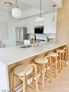 kitchen with a breakfast bar, sink, white cabinetry, hanging light fixtures, and kitchen peninsula