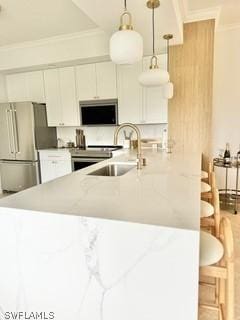 kitchen featuring sink, pendant lighting, stainless steel appliances, light stone countertops, and white cabinets