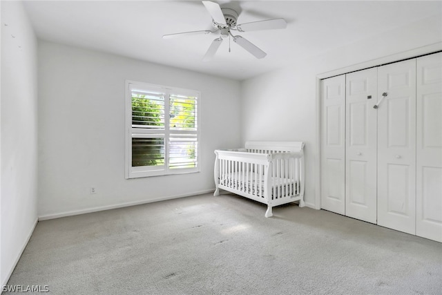 unfurnished bedroom featuring a nursery area, ceiling fan, light carpet, and a closet