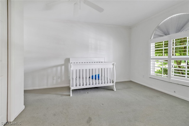 unfurnished bedroom with crown molding, ceiling fan, light carpet, and a crib