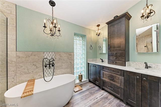 bathroom featuring tile walls, vanity, an inviting chandelier, hardwood / wood-style flooring, and a washtub