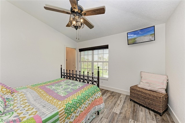 bedroom with ceiling fan, a textured ceiling, light hardwood / wood-style flooring, and lofted ceiling