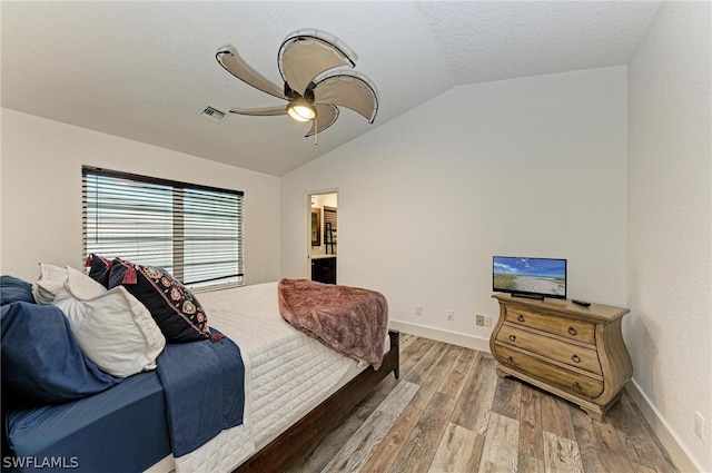 bedroom with a textured ceiling, lofted ceiling, ceiling fan, ensuite bathroom, and hardwood / wood-style flooring