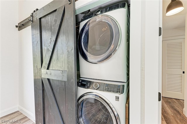 washroom featuring stacked washer and clothes dryer, hardwood / wood-style floors, and a barn door