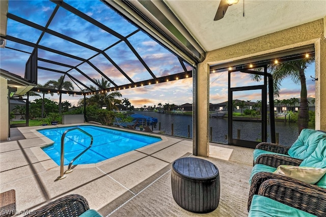 pool at dusk featuring ceiling fan, a patio, glass enclosure, and a water view