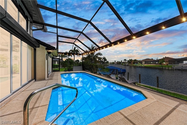 pool at dusk featuring glass enclosure, a water view, and a patio