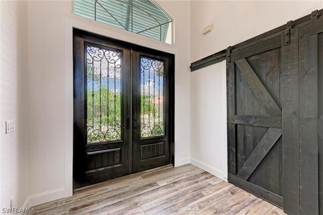 foyer entrance with a barn door, a healthy amount of sunlight, light hardwood / wood-style flooring, and french doors