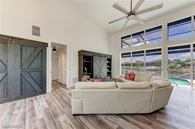 living room featuring a barn door, high vaulted ceiling, ceiling fan, and hardwood / wood-style flooring