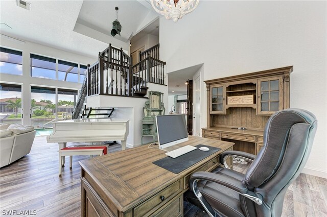 office with light hardwood / wood-style flooring, a high ceiling, and a notable chandelier