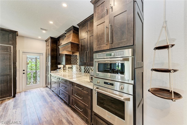 kitchen with light stone counters, tasteful backsplash, a textured ceiling, double oven, and light wood-type flooring