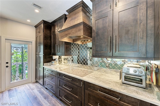 kitchen with premium range hood, light hardwood / wood-style floors, decorative backsplash, light stone countertops, and black electric stovetop