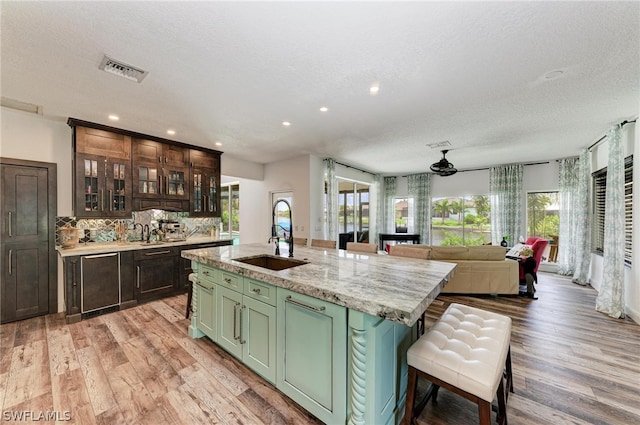 kitchen featuring green cabinetry, a kitchen island with sink, sink, and a wealth of natural light